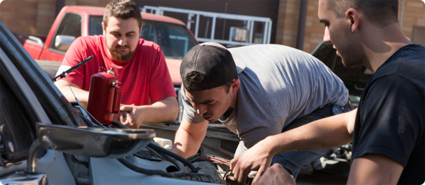 三个学汽车的学生在检查一辆汽车的发动机，以评估必要的维修.